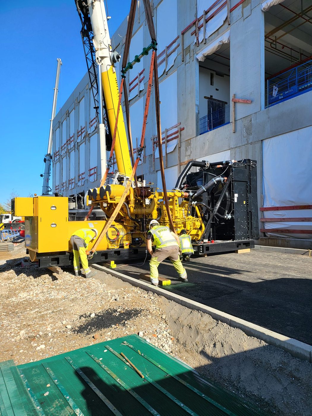 Pose d'un groupe électrogène industriel par grue sur un site neuf.